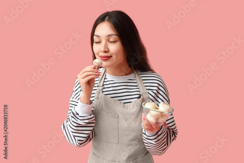 Beautiful young happy Asian woman with bowl of fresh mushrooms on pink backgr...