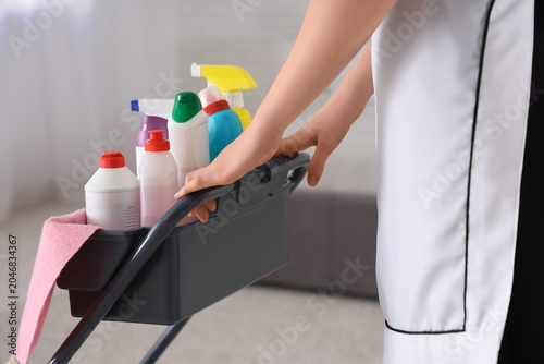 Schilderij op canvas Young chambermaid carrying trolley with cleaning supplies in hotel room, closeup