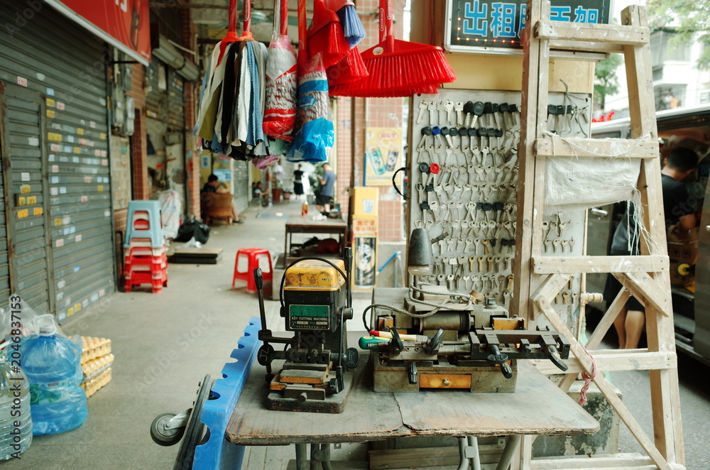 Fototapeta premium Street-side key-cutting shop with tools, ladder, and hanging goods in an urban alley in China