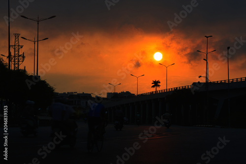 Obraz na plátně Dramatic orange sunset over Saigon Bridge with silhouettes of commuters, Ho Chi