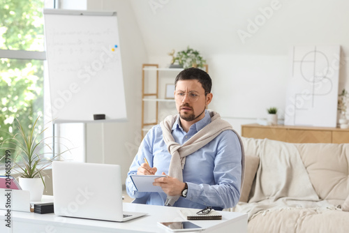 Confused young male teacher with laptop and notebook giving online lesson at ...