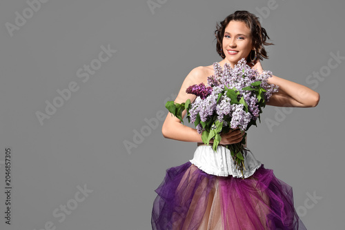 Happy young woman with bouquet of blooming lilac flowers on grey background