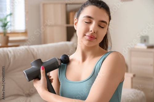 Cuadro en lienzo Sporty young woman with percussive massager at home, closeup