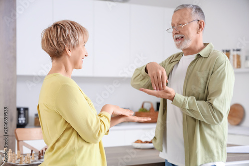 Mature deaf mute man with his wife using sign language in kitchen