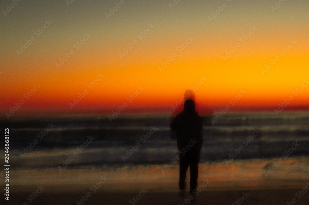 Fototapeta premium Blurry silhouette of person on the beach at sunrise