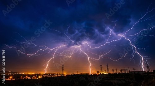 Quadro su tela Multiple simultaneous lightning strikes illuminating an electrical substation an