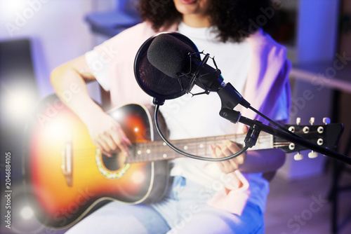 Microphone against woman playing guitar in recording studio, closeup