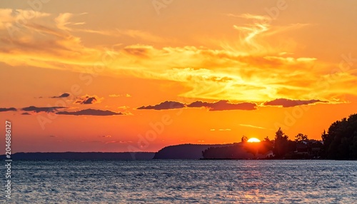 A vibrant sunset paints the sky with fiery hues over tranquil water and a distant shoreline