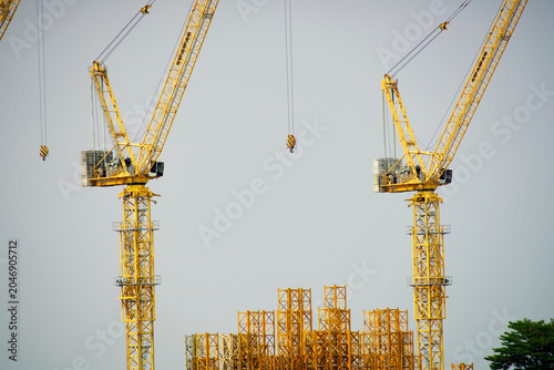Two Construction Cranes with a Building Framework Under Development Against Gray Sky