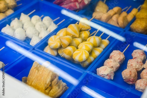 Assorted colorful Chinese fish balls on skewers with striped sea urchin buns inside blue plastic trays at local street food stall in Taipa Macau
