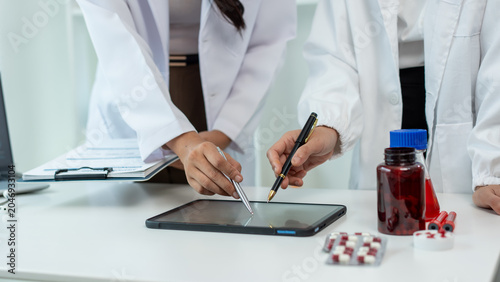 Medical professionals in white lab coats reviewing data on a tablet beside medicine bottles and pills on a clinic desk, showing teamwork, healthcare planning, and modern hospital work.