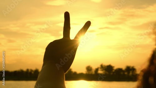 Canvastavla A hand forms the V-sign against a golden sky, evoking peace, victory, and dreams