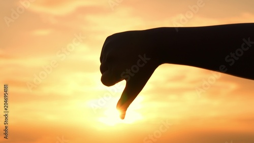 Foto With a thumbs-down sign against the sunset, this image conveys rejection and disagreement