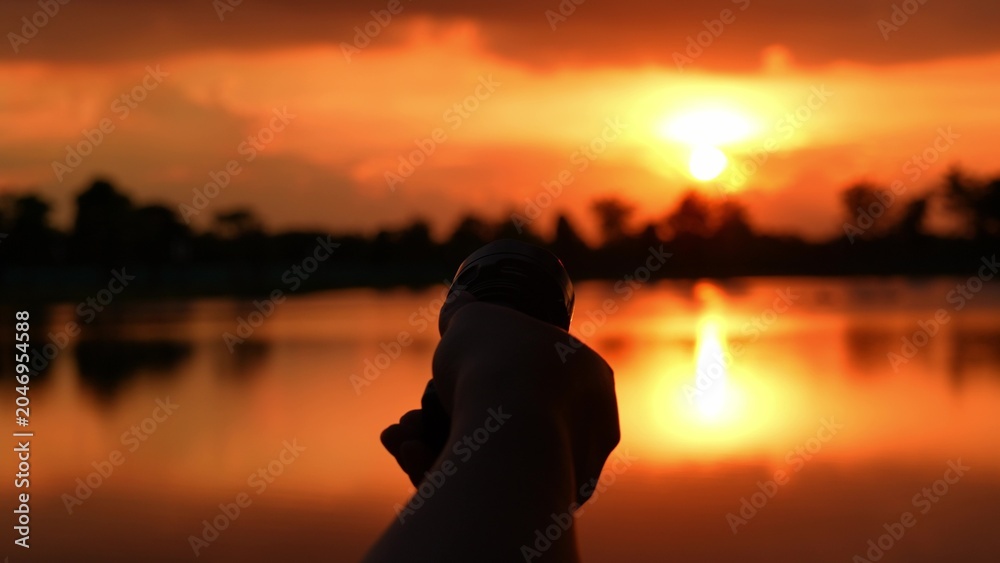 Fototapeta premium A hand points a flashlight at the sunset, representing exploration, curiosity, the pursuit of answers, determination to illuminate uncertainty, and the interplay of technology and natural beauty. 