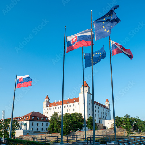 Photography Slovak and European Union flags waving in front of Bratislava Castle under a clear blue sky