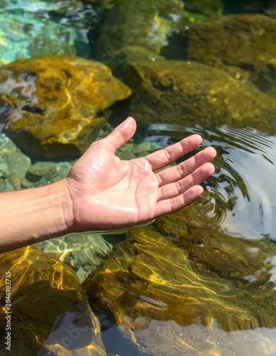 A hand reaching out over clear water with rocks