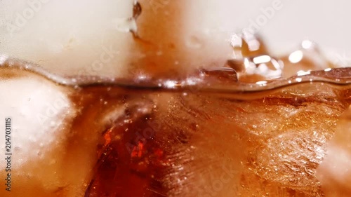 Slow motion closeup pouring cola with ice cubes and bubbles, soft drink texture