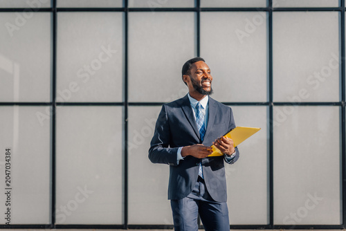 Принти на полотні Smiling businessman holding folder looking confidently forward