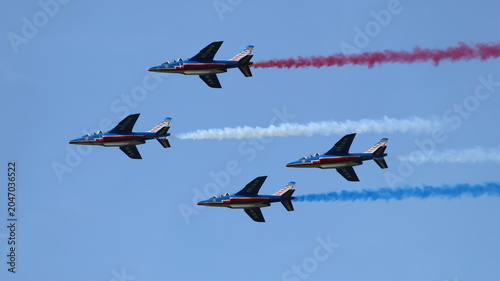 View of Patrouille de France aerobatic team flying in formation and trailing red, white, and blue smoke against a clear blue sky during an airshow La Ferte-Alais, Ile-de-France, France.