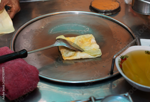 The roti sheets are being fried in a stainless steel pan.