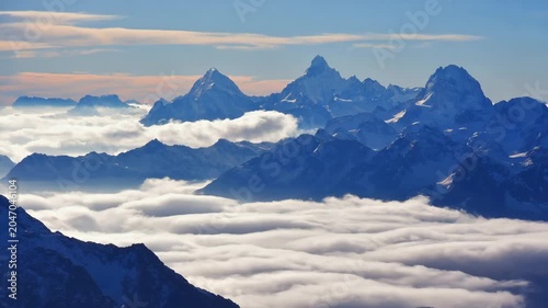 Scenic view of snow-covered mountain peaks rising above a sea of clouds at sunrise