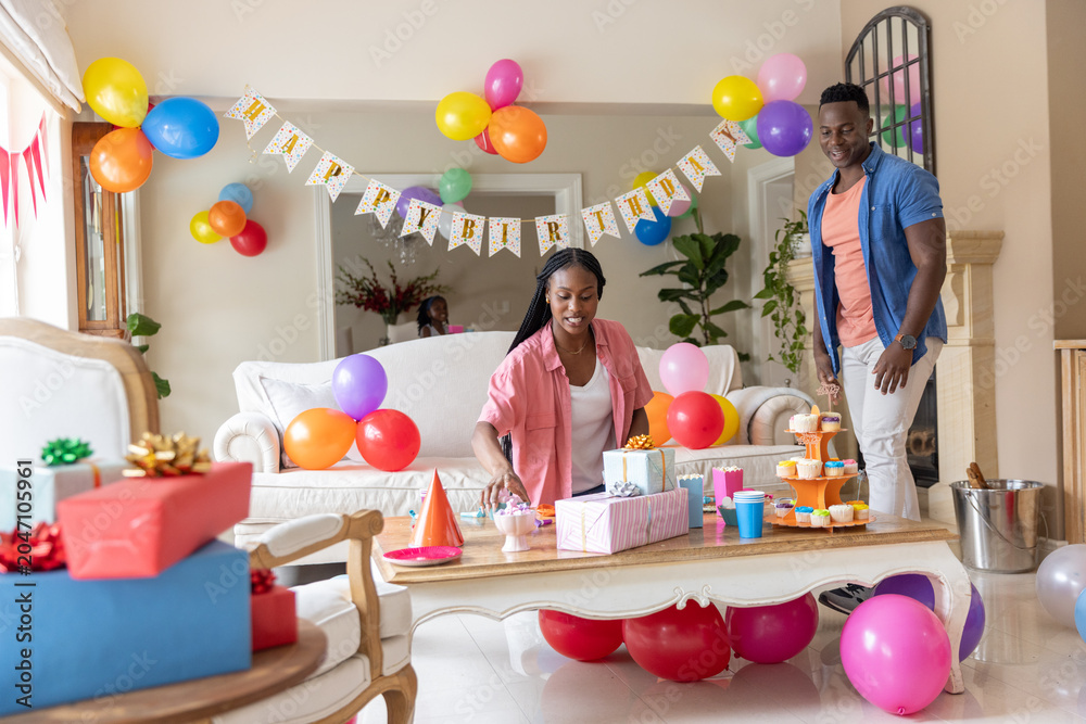 Obraz premium African American couple arranging Happy Birthday banner and balloons on coffee table in living room