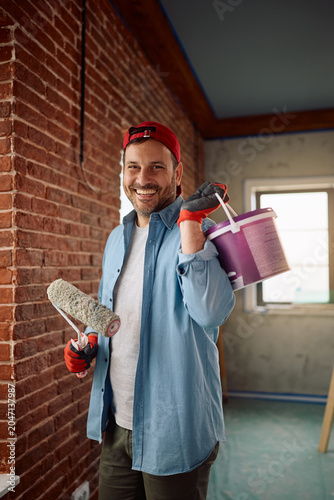 Happy man painting walls while renovating his apartment and looking at camera.