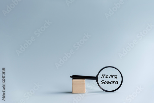 Schilderij op canvas A magnifying glass with the text 'Moving Forward' is placed next to a small wooden block on a light blue background