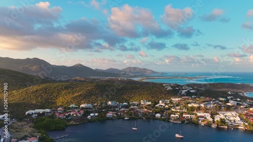 Drone aerial view of Oyster Pond bay on the border of Sint Maarten and Saint Martin. Tropical island landscape features luxury coastal houses and boats anchored in the calm harbor.