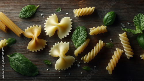 Bow tie pasta fusilli penne mint leaf basil leaf raw pasta dry pasta wooden background scattered pasta culinary ingredients Italian cuisine food