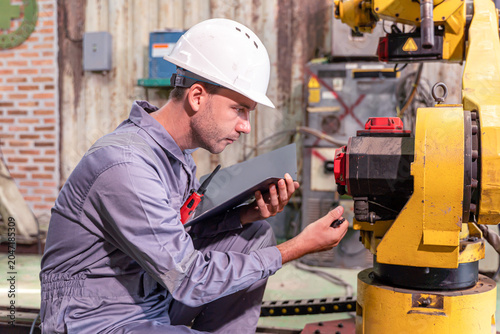 Closeup white male engineer checking for repair welding robotics automatic arms machine in factory automotive industrial.