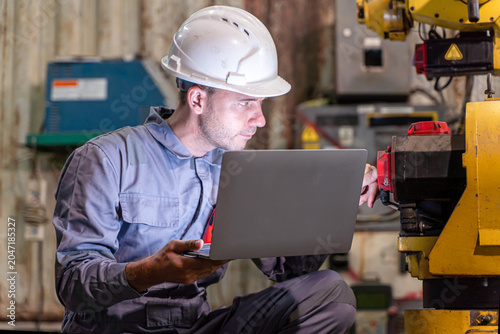 Closeup white male engineer use laptop checking for repair welding robotics automatic arms machine in factory automotive industrial.