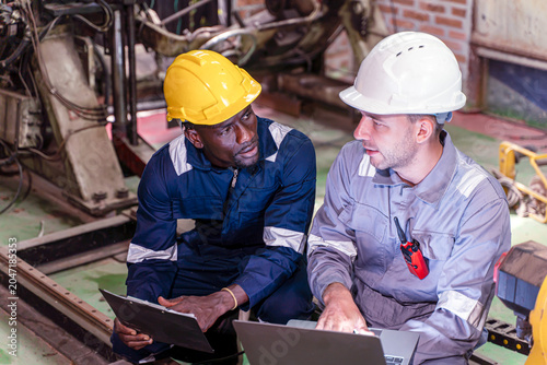 Closeup two engineer work collaborating with laptop and clipboard while inspecting industrial machinery