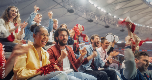 Slika na platnu A Black Woman in Yellow and a White Man With Red Cheek Paint Cheer With Soccer Fans From Stadium Seats, Waving Scarves as Nearby Supporters Beat Drums in a Championship Match