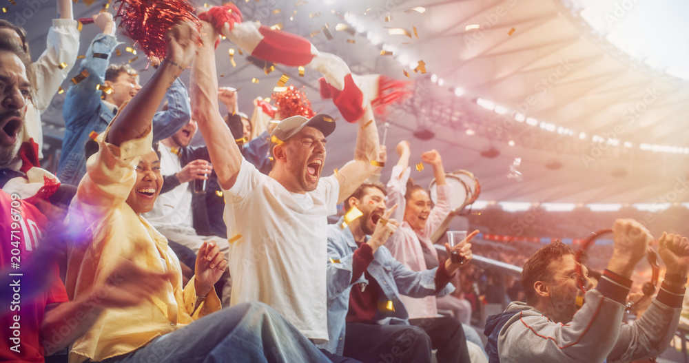 Naklejka premium Diverse Soccer Supporters Surge Upright in Stadium Seats During a Football Championship, Shouting in Disbelief, Relief and Victory While a Red Scarf Swings, a Tambourine Shakes and Confetti Falls.