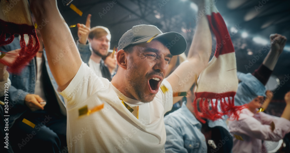 Naklejka premium Close Portrait of White Male Soccer Football Fans in Championship Stadium Stands, Arms and Scarves Raised to Cheer, Happy, Smiling, Excited as Red and Gold Confetti Falls During a Cup Match.