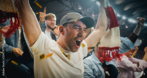 Close Portrait of White Male Soccer Football Fans in Championship Stadium Stands, Arms and Scarves Raised to Cheer, Happy, Smiling, Excited as Red and Gold Confetti Falls During a Cup Match.