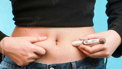 Determined female patient uses medical injection pen on stomach belly abdomen fat during hopeful healthy weight loss journey to treat body