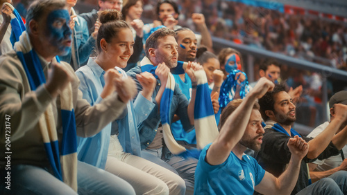 Diverse Crowd of Excited Male and Female Fans With Painted Faces and Blue Scarves Watching a Tense Soccer Football Championship Match in Stadium Stands, Happy Smiling Supporters Cheer for Their Team.