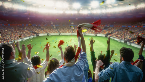 Golden Confetti Falling Over Diverse Excited Fans Waving a Red Scarf and Raising Hands to Cheer Their Winning Team During a Soccer Championship, Happy Crowd Celebrating Victory at a Football Stadium.