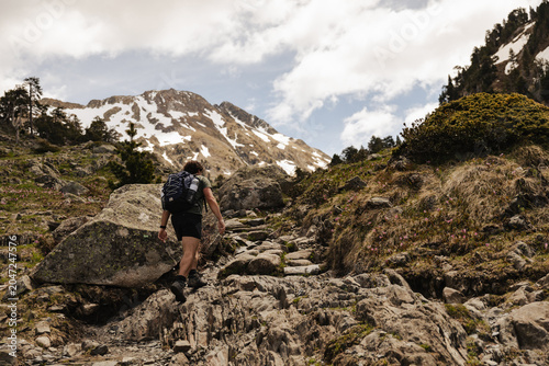 Obraz na płótnie Male hiker with backpack walking along a rocky mountain trail surrounded by pine trees and alpine vegetation in the Spanish Pyrenees