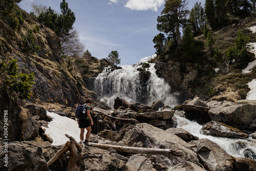 Foto Male hiker standing on rocks in front of a powerful mountain waterfall in the Spanish Pyrenees