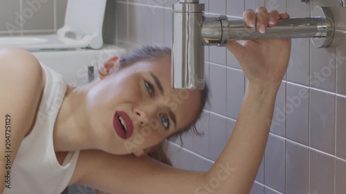 Worried young woman looking at leaking pipe under bathroom sink home emergency