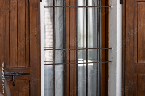 Iron security bars on a residential window with wooden shutters, symbolizing home protection, burglary prevention, residential security and property safety.
