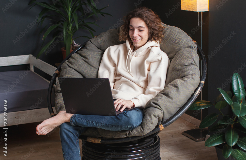 Fototapeta premium Smiling young man sitting on sofa with laptop at home