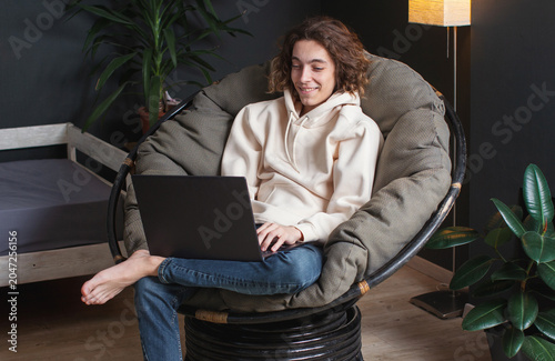 Foto Smiling young man sitting on sofa with laptop at home