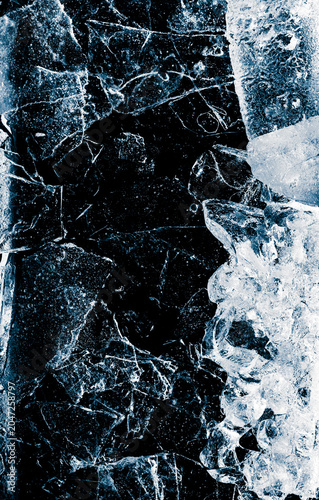 Broken thin ice shards with space for copy. Crushed natural textured ice on a black background, close-up.