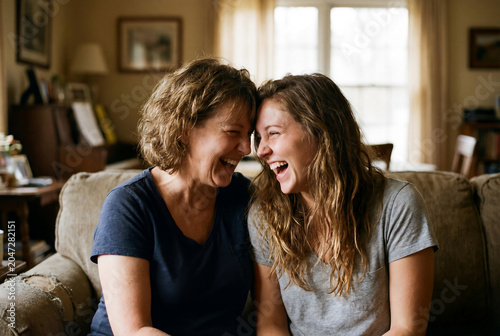 Happy middle aged mother and adult daughter laughing together on sofa at home as symbol of generational bonding female friendship senior care insurance and family support lifestyle