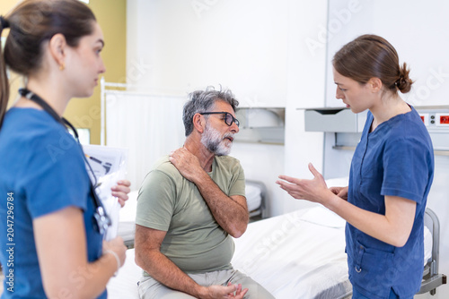 Pain in the shoulder. Upper arm pain, senior man with muscles problem, healthcare concept. Female doctor consulting elderly patient sitting on clinic bed and holding painful arm with another hand.