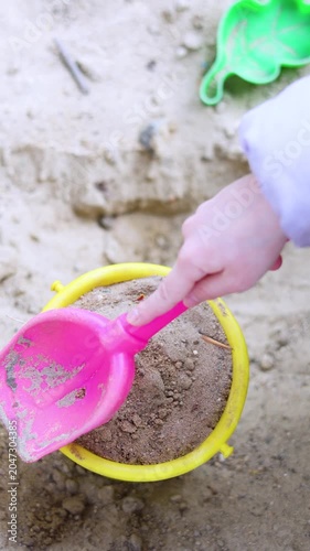 Delight in the joy of childhood as little hands scoop sand from the sandbox and pour it into a bright bucket. Watch their creativity unfold amidst laughter and carefree play. Vertical 4k footage.